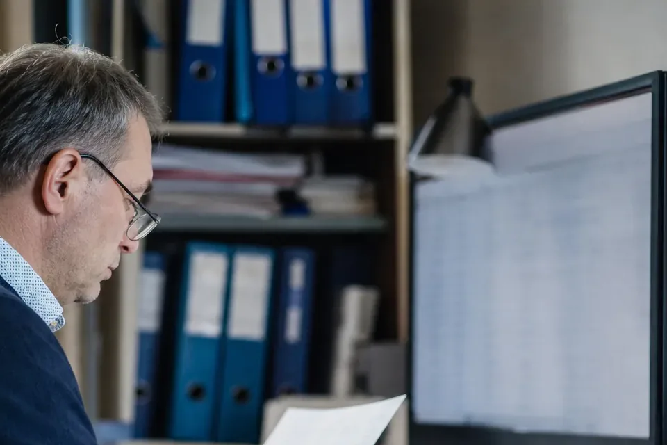 Księgowy porównuje dane kontrahenta z dokumentu z profilem firmy na monitorze
